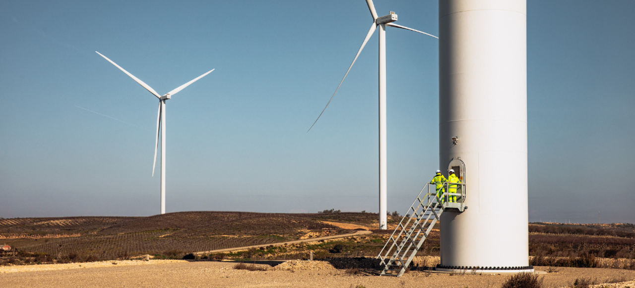 Workers entering the base of a turbine with 2 turbines in the distance