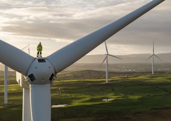Turbine technician standing on top of turbine at dusk in green fields
