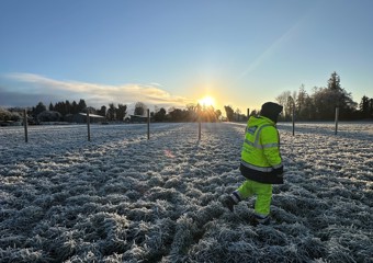 Worker in front of frosty field at sunrise